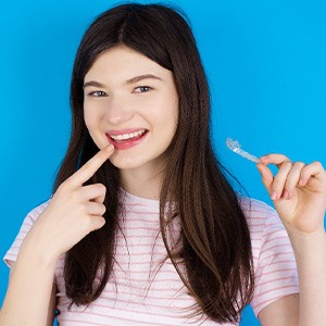Teenager in striped t-shirt holding Invisalign and pointing to her teeth