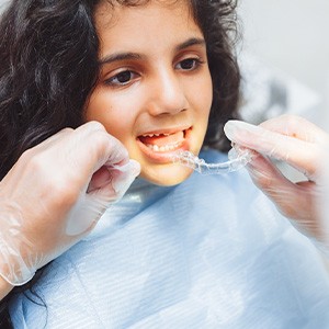 Gloved hands placing Invisalign over a girl’s lower arch
