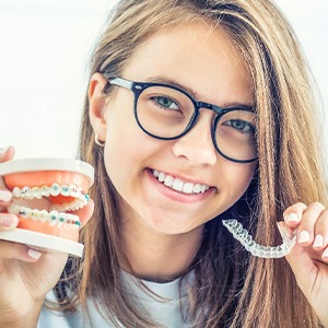 Teen with glasses holding sample jaw with braces in one hand and Invisalign in the other