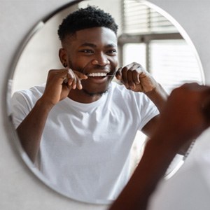 Man smiling while flossing teeth in bathroom