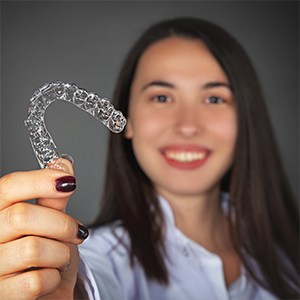 Young woman holding up an Invisalign Teen aligner tray