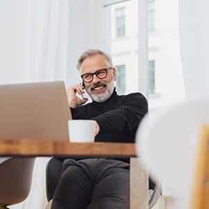 Man smiling while talking on phone and working on laptop