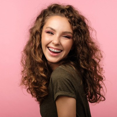Teen girl with braces smiling against pink background
