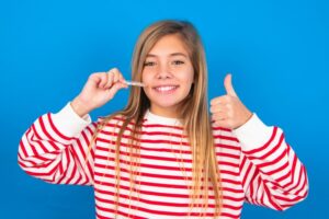 Teen girl holding clear aligner and giving a thumbs up. 