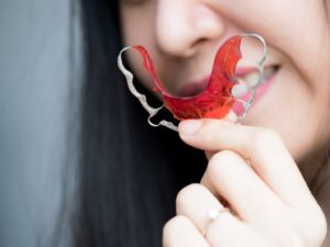 Woman holding up red retainer in foreground.